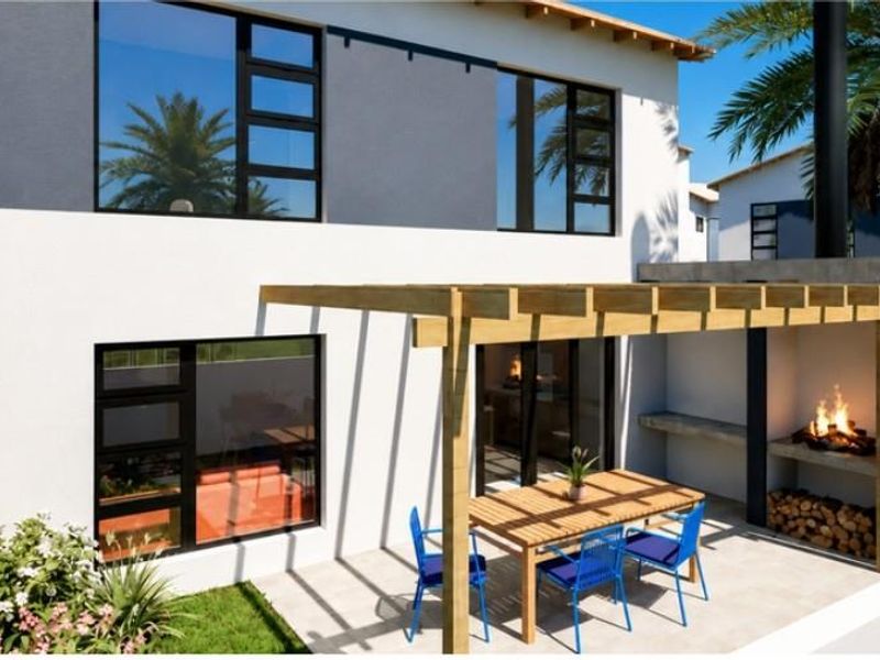 Rear exterior view of a townhouse featuring a tiled patio, timber pergola, and a built-in braai area overlooking a private garden.