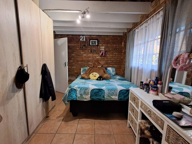 A cozy bedroom featuring exposed brick walls, timber ceiling beams, tiled flooring, and a built-in wardrobe.