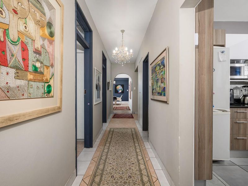 A well-lit hallway featuring tiled flooring, a decorative crystal chandelier, and an arched transition leading to adjacent living spaces and a modern kitchen.