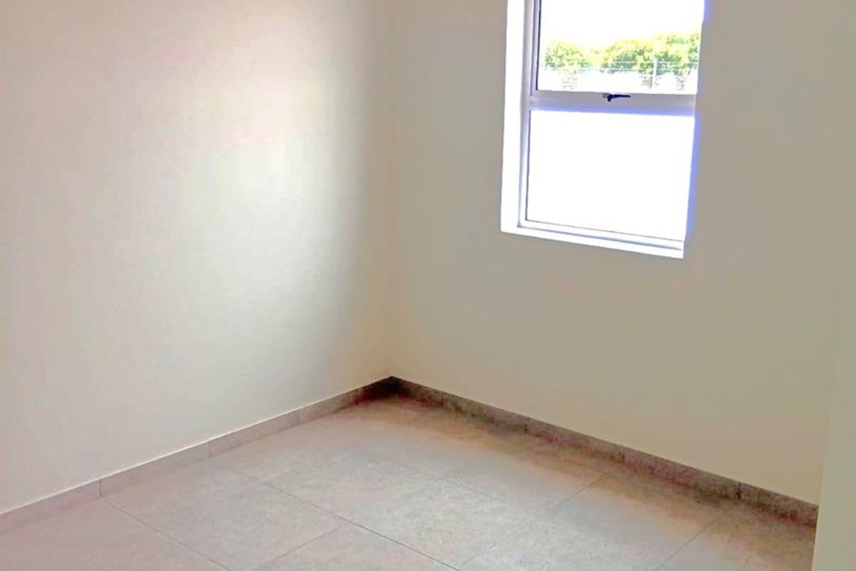 A clean, empty bedroom featuring neutral tiled flooring and a single window, providing a blank canvas for interior design.