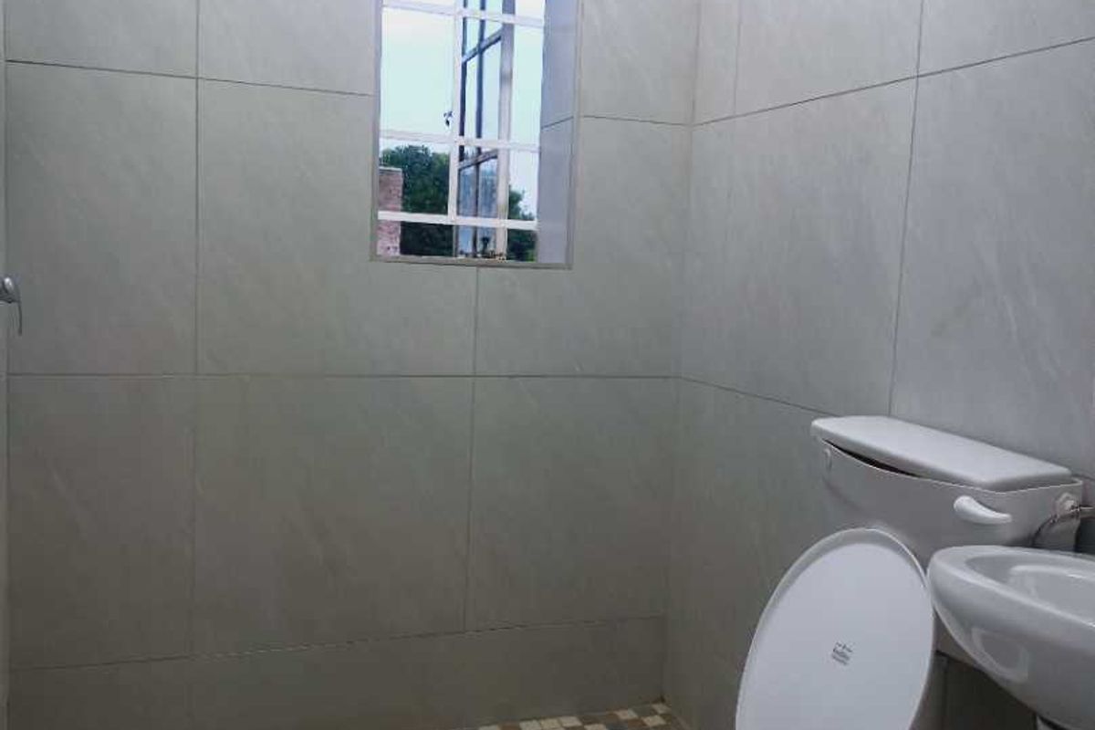 A functional bathroom featuring a walk-in shower area, pedestal basin, and toilet with neutral wall tiling and a small window for natural light.