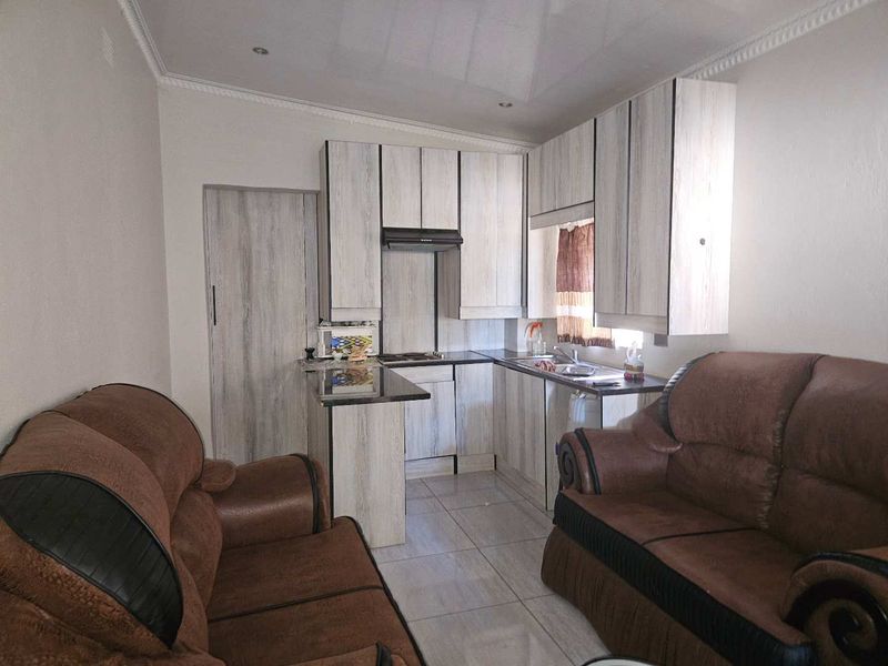 Open plan kitchen and living area featuring light wood-look cabinetry, integrated hob, extractor fan, and tiled flooring throughout.