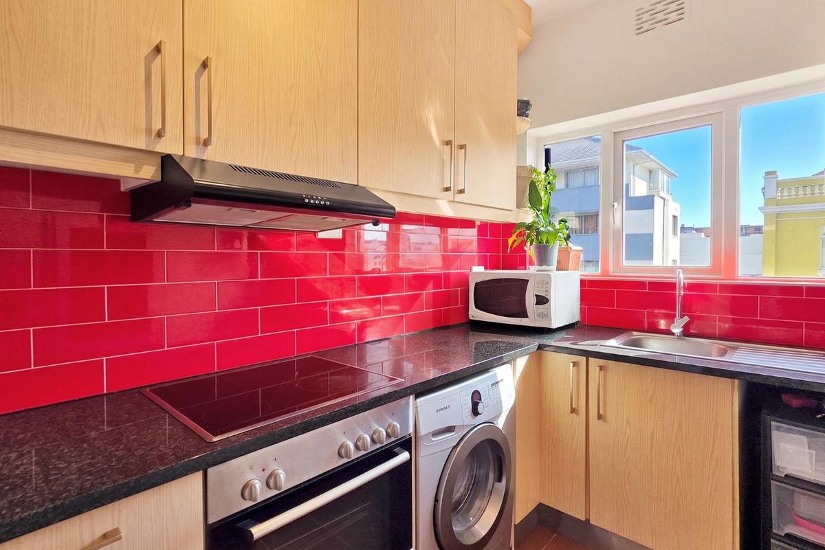 A functional kitchen featuring light wood cabinetry, a striking red subway tile backsplash, black granite countertops, and integrated appliances including an oven and washing machine.
