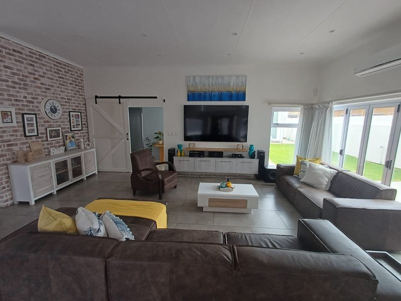 Spacious living room featuring an exposed brick accent wall, tiled flooring, recessed lighting, and large glass sliding doors providing access to the garden.