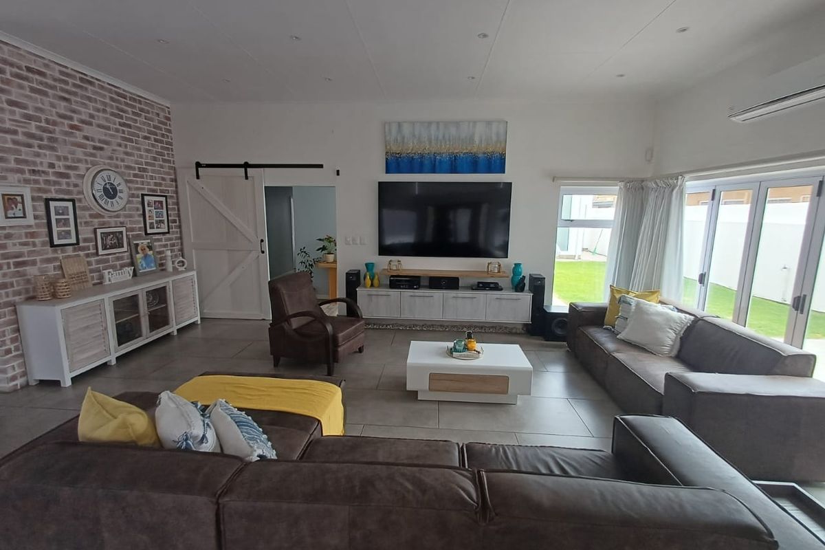 Spacious living room featuring an exposed brick accent wall, tiled flooring, recessed lighting, and large glass sliding doors providing access to the garden.