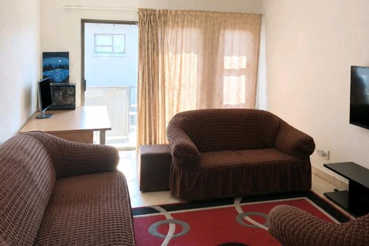 A living room featuring tiled flooring, a ceiling-mounted spotlight fixture, and a sliding glass door providing access to an outdoor area.