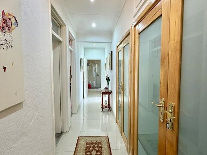 A bright, well-maintained hallway featuring tiled flooring, recessed downlighting, and multiple frosted glass timber doors providing access to adjacent rooms.
