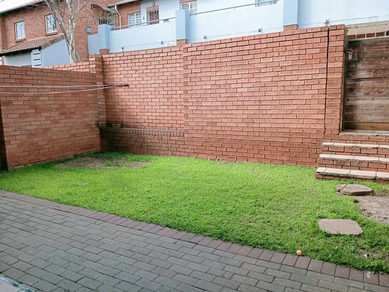A private rear courtyard featuring a paved patio area, a small lawn, and high brick boundary walls with a timber access gate.