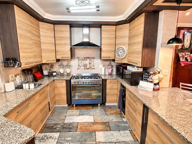 A well-appointed kitchen featuring granite countertops, light wood-finish cabinetry, a gas hob with extractor fan, and distinctive stone-look floor tiling.