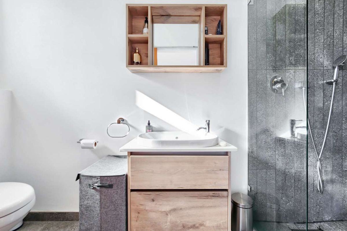 Modern bathroom featuring a wood-finish vanity with vessel sink, wall-mounted storage cabinet, and a spacious walk-in shower with textured stone-look tiling.