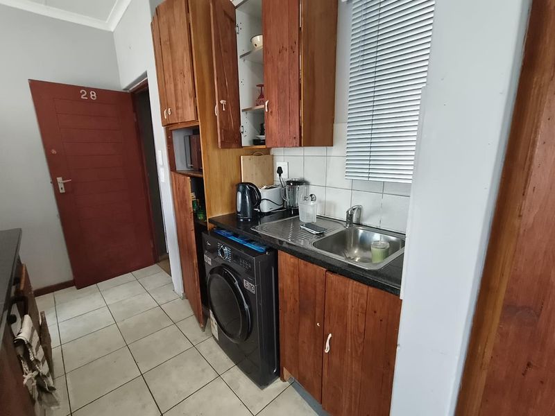Compact kitchen featuring wooden cabinetry, stainless steel sink, and tiled flooring, offering a functional layout with space for a washing machine.