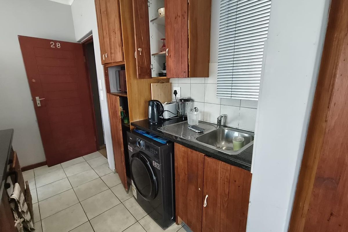 Compact kitchen featuring wooden cabinetry, stainless steel sink, and tiled flooring, offering a functional layout with space for a washing machine.