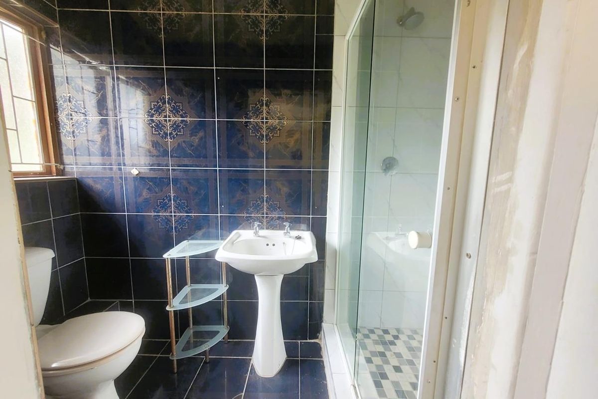 A compact bathroom featuring a pedestal basin, a toilet, and a glass-enclosed shower with dark decorative wall tiling.