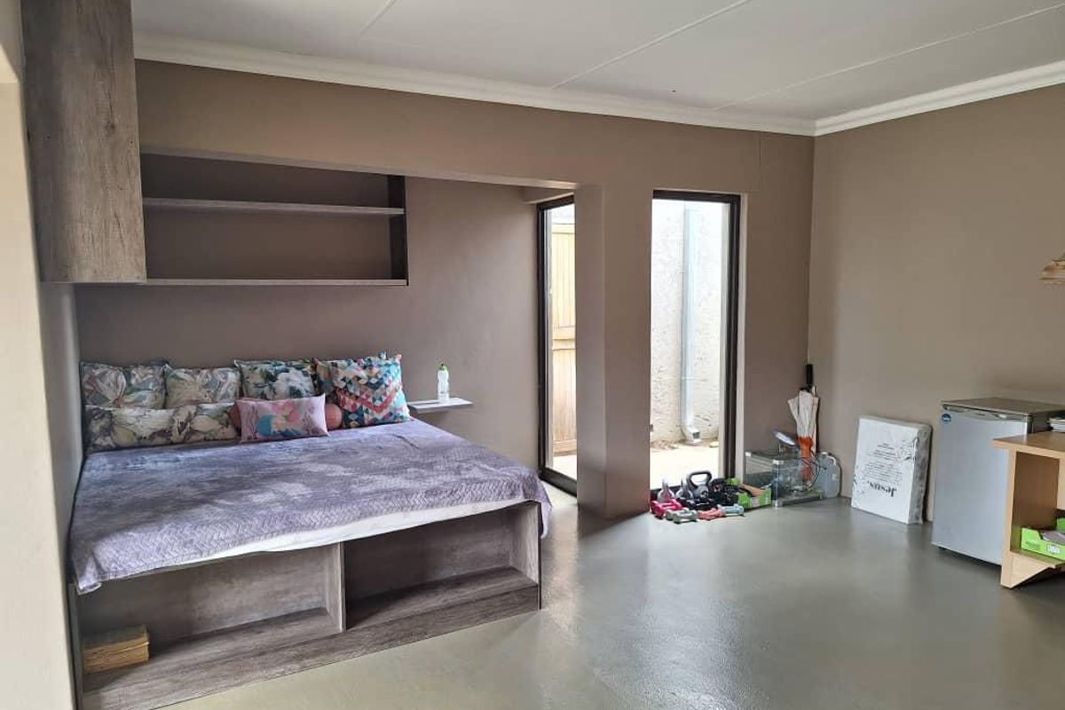 A bedroom featuring a built-in platform bed frame with integrated shelving and direct access to an outdoor area through a glass door.
