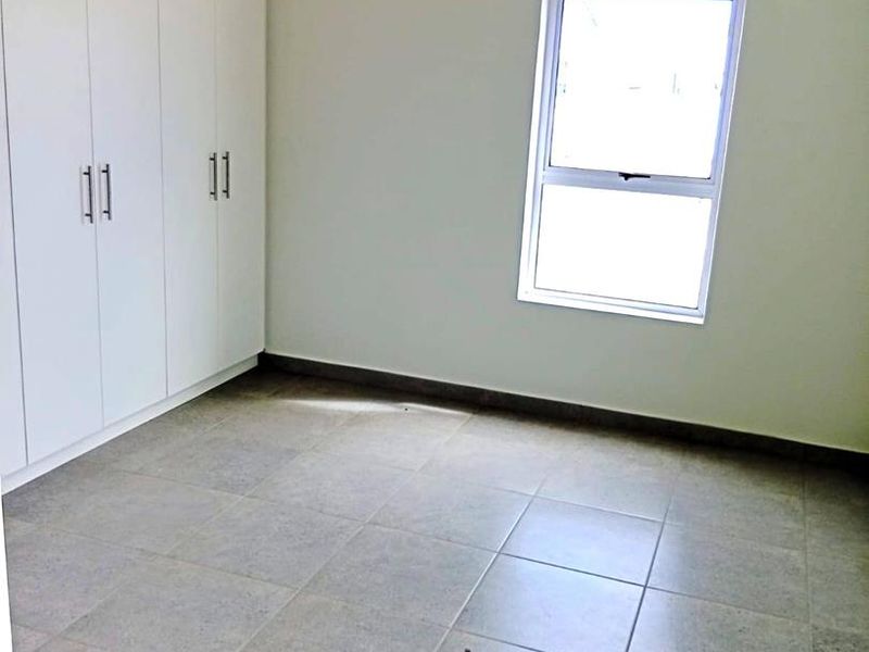 A clean, empty bedroom featuring neutral tiled flooring, built-in white cupboards, and a single window providing natural light.