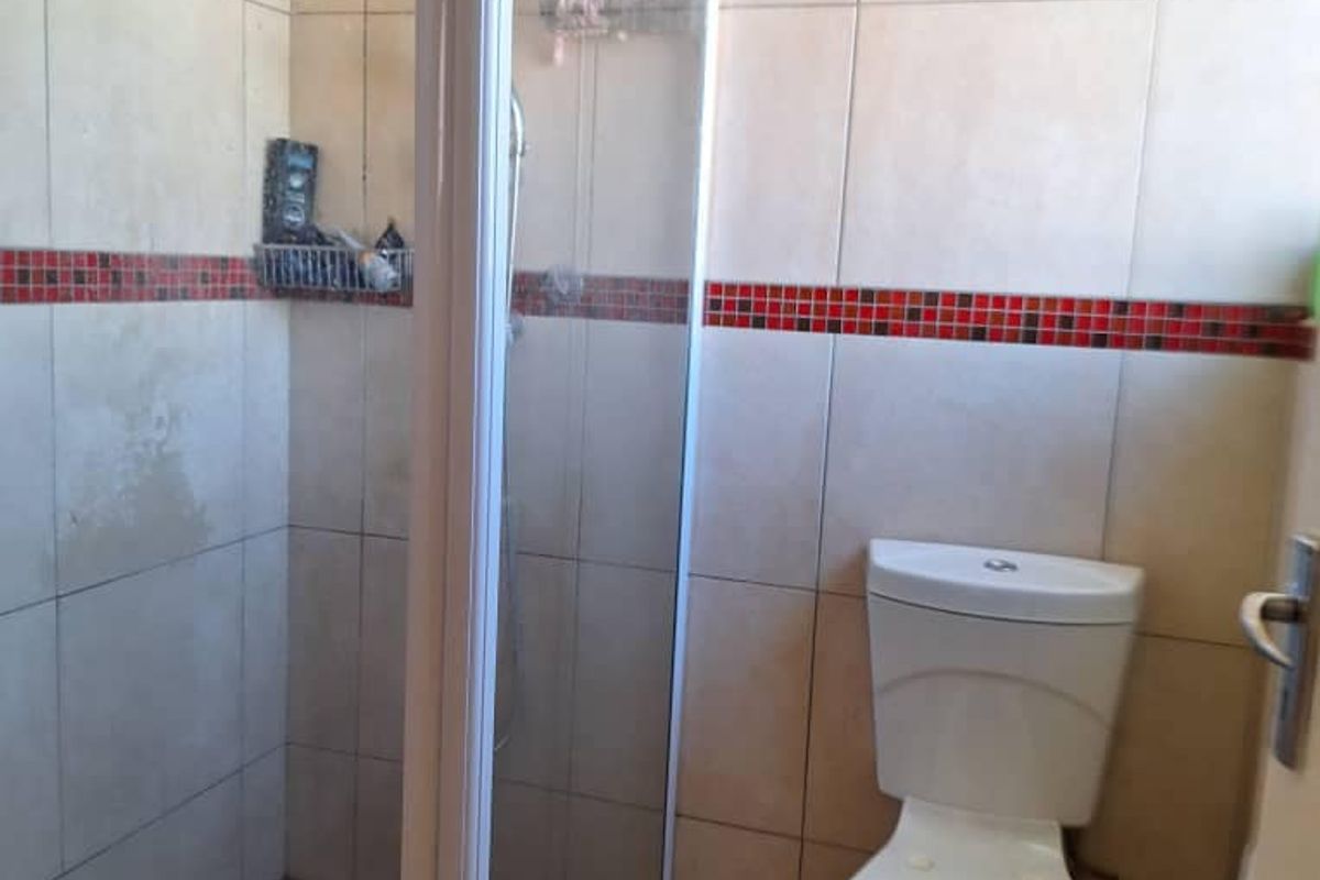 A functional bathroom featuring a glass-enclosed shower stall and a standard white toilet with decorative red mosaic tile accents.