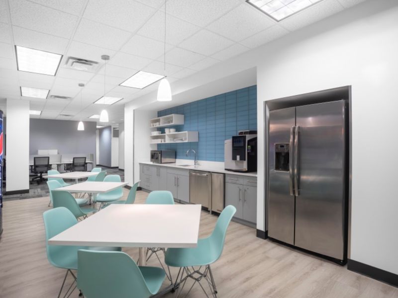 Modern office breakroom featuring built-in cabinetry, stainless steel appliances, a tiled backsplash, and a clean, functional layout for staff use.