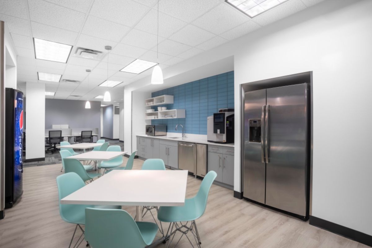 Modern office breakroom featuring built-in cabinetry, stainless steel appliances, a tiled backsplash, and a clean, functional layout for staff use.