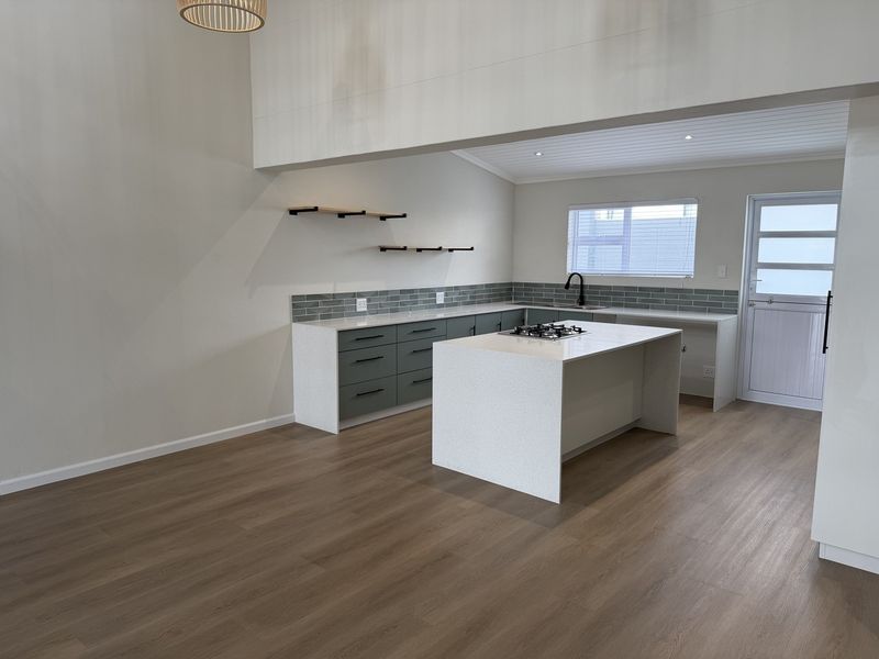Modern, newly renovated kitchen featuring a central island with gas cooktop, quartz countertops, subway tile backsplash, and sleek cabinetry in an open-plan layout.