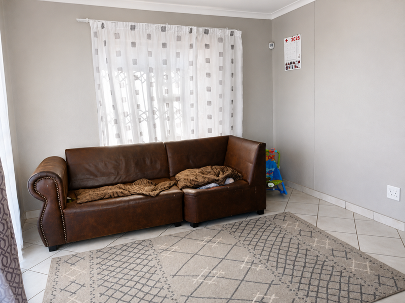 A living room featuring neutral wall paint, ceramic tiled flooring, and a window fitted with a curtain rod.