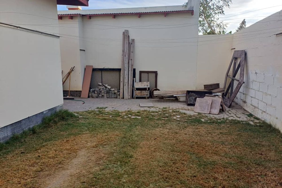A rear outdoor area featuring a paved section, perimeter boundary walls, and a lawn area requiring maintenance.