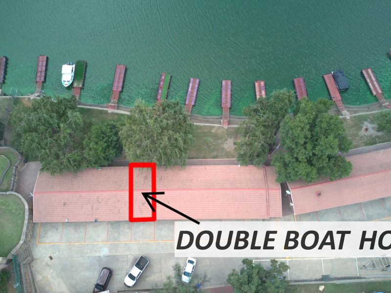 Aerial view of a property featuring a double boat house with a tiled roof, adjacent to a concrete driveway and multiple waterfront boat jetties.