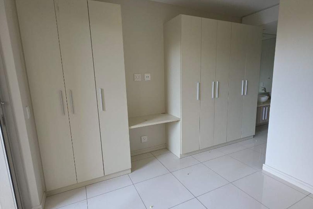 A bright, empty bedroom featuring extensive built-in cabinetry, a integrated desk area, and clean tiled flooring throughout.