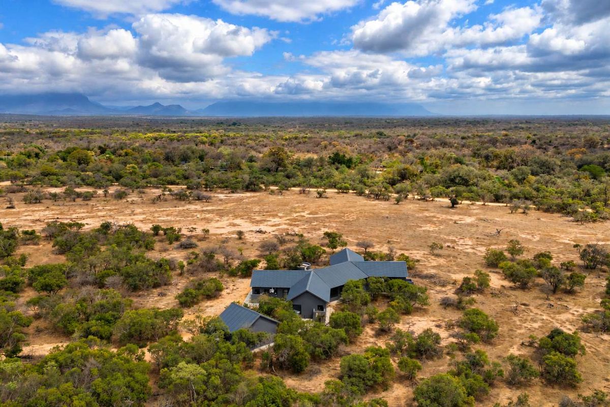 Aerial view of a modern multi-wing residence with a dark metal roof, situated within a vast, natural bushveld landscape.