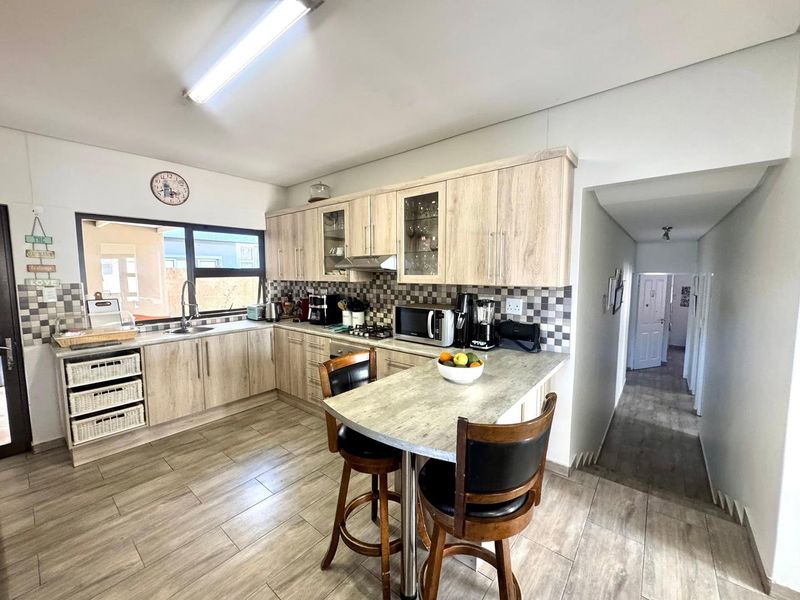 A functional kitchen featuring light wood-tone cabinetry, a breakfast bar, tiled backsplash, and integrated cooking appliances, leading into a hallway.