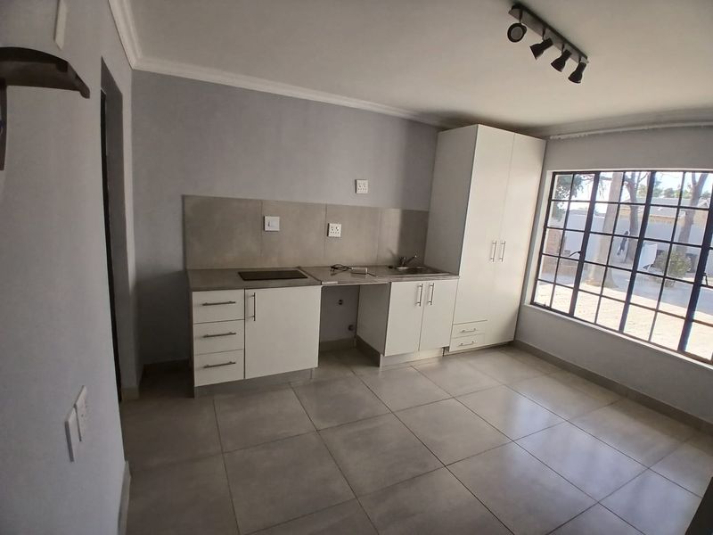 A clean, modern kitchen featuring white built-in cabinetry, tiled flooring, a built-in hob, and a stainless steel sink with a tiled backsplash.