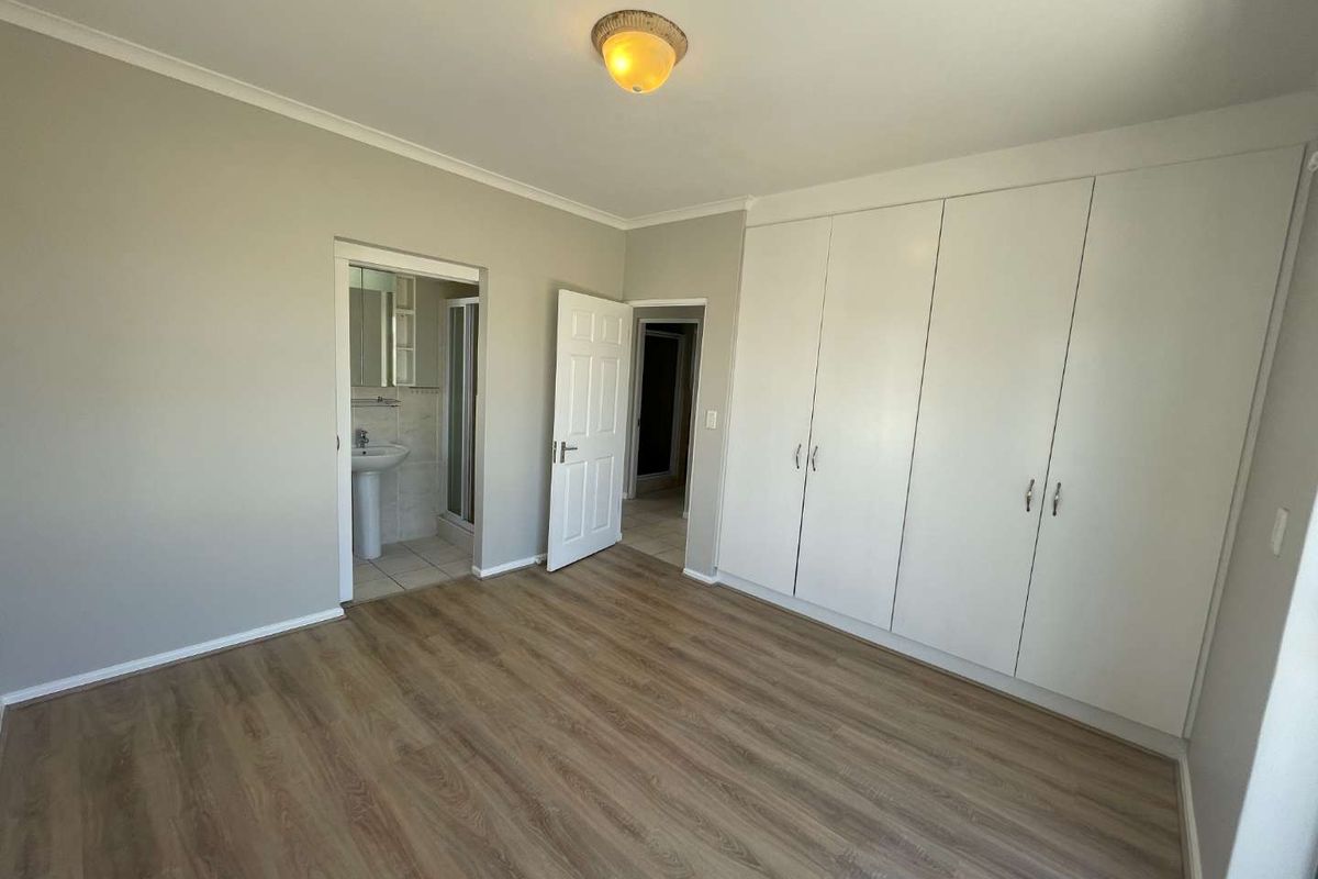 Spacious bedroom featuring modern laminate flooring, extensive built-in cupboards, and direct access to an en-suite bathroom.