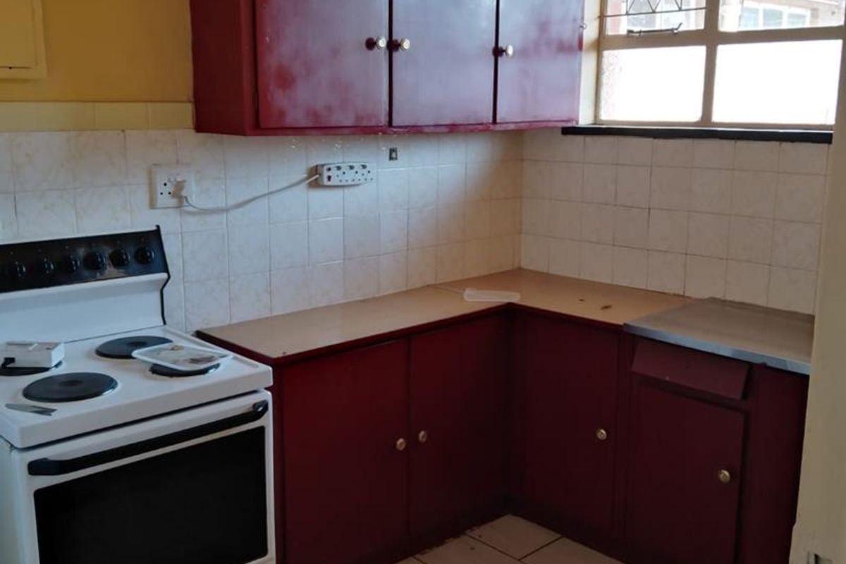A compact kitchen featuring dated red cabinetry, a tiled backsplash, and a freestanding stove, offering a functional layout with potential for modernization.