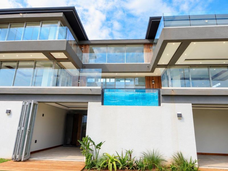 Modern multi-story rear elevation featuring glass balconies, a raised swimming pool with a glass edge, and seamless indoor-outdoor flow through bi-fold doors.