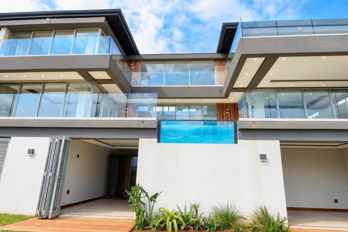Modern multi-story rear elevation featuring glass balconies, a raised swimming pool with a glass edge, and seamless indoor-outdoor flow through bi-fold doors.