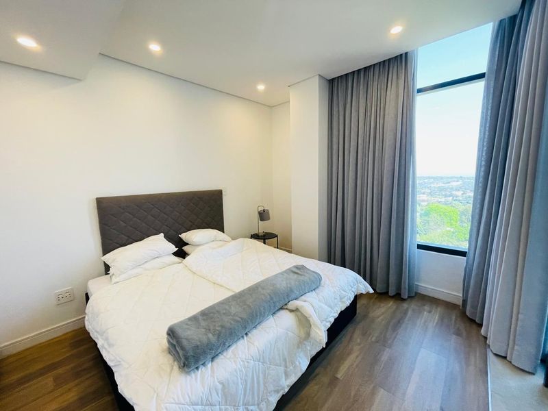 Modern bedroom featuring laminate flooring, recessed lighting, and a large floor-to-ceiling window with expansive views and full-height curtains.