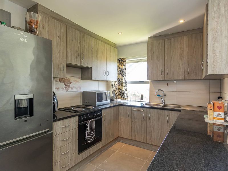 A modern kitchen featuring wood-grain cabinetry, granite countertops, a double basin sink, and integrated electric cooking appliances.