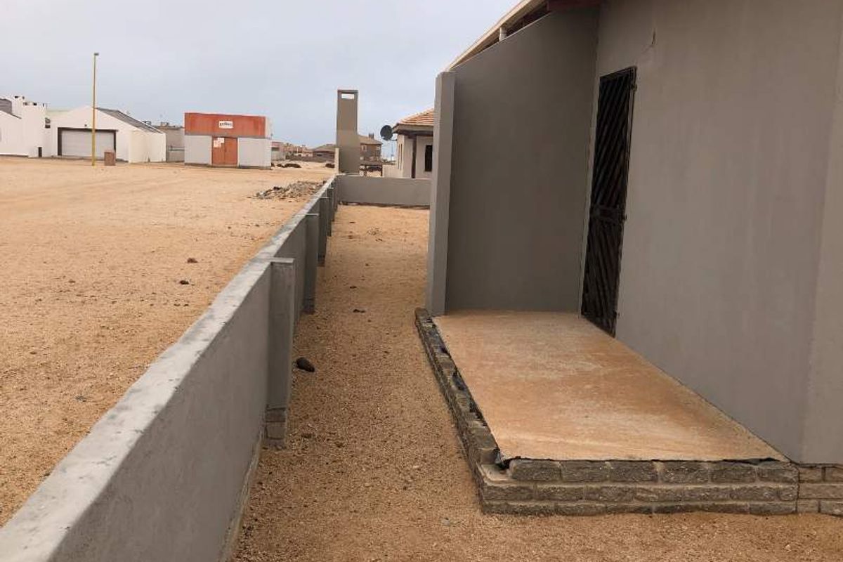 Side exterior view of the property featuring a concrete boundary wall, a small paved entrance area, and a metal security gate.