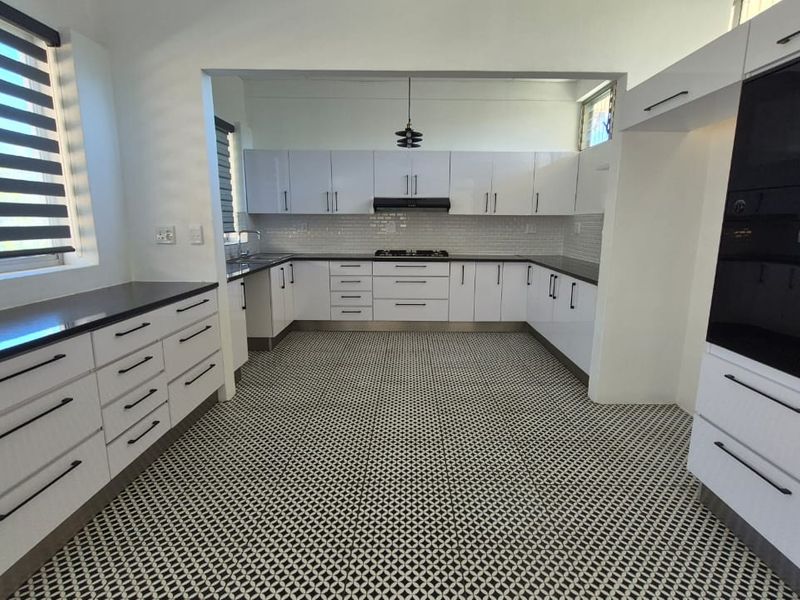 Modern, spacious kitchen featuring white cabinetry, dark countertops, a gas hob, built-in oven, and distinctive patterned floor tiles.