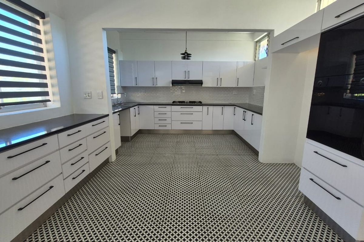 Modern, spacious kitchen featuring white cabinetry, dark countertops, a gas hob, built-in oven, and distinctive patterned floor tiles.