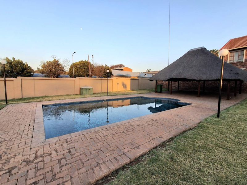 Outdoor pool area featuring a swimming pool, brick paved surround, and a traditional thatched lapa, set within a walled garden.