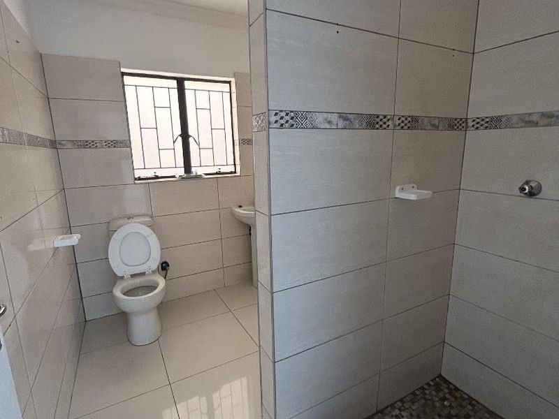 A clean, functional bathroom featuring a tiled shower enclosure, pedestal basin, and toilet with neutral wall and floor tiles.