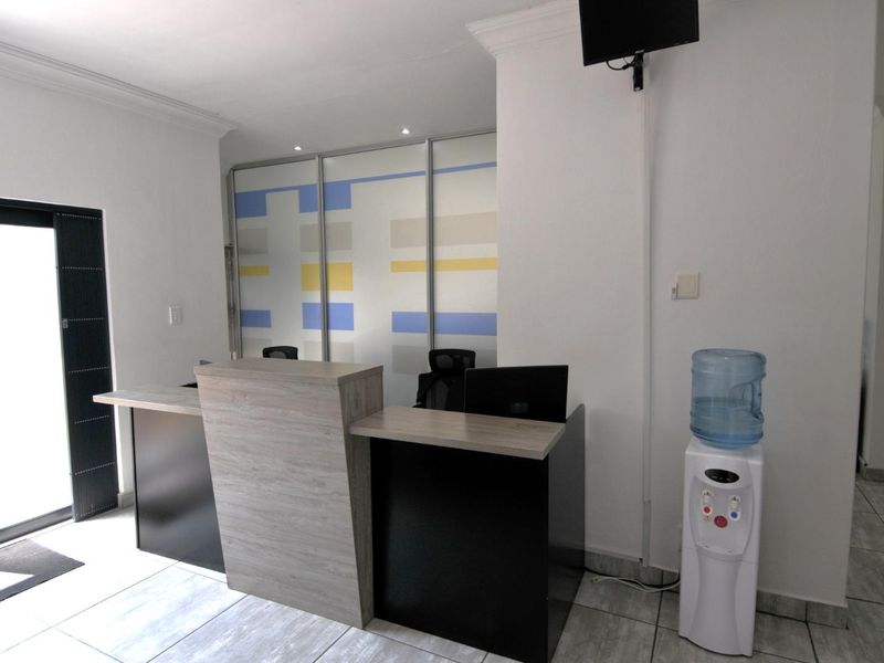 A professional office reception area featuring a modern built-in desk, tiled flooring, and a decorative sliding glass partition.