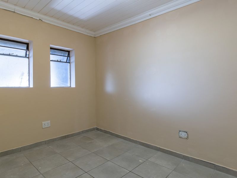 An empty bedroom featuring tiled flooring, a timber ceiling with coving, and dual windows, providing a blank canvas for renovation or interior design.