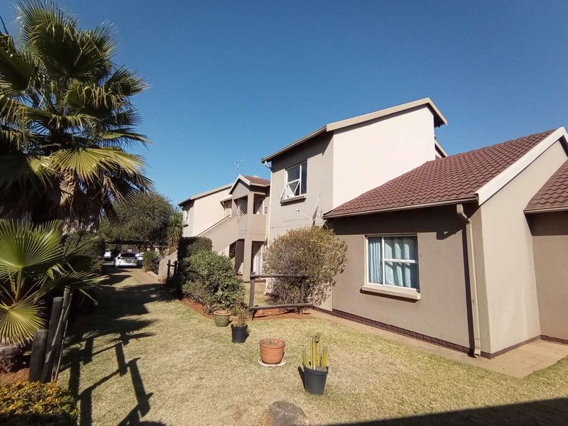 Rear exterior view of the townhouse complex featuring tiled roofing, plastered walls, and a paved walkway alongside a landscaped garden area.