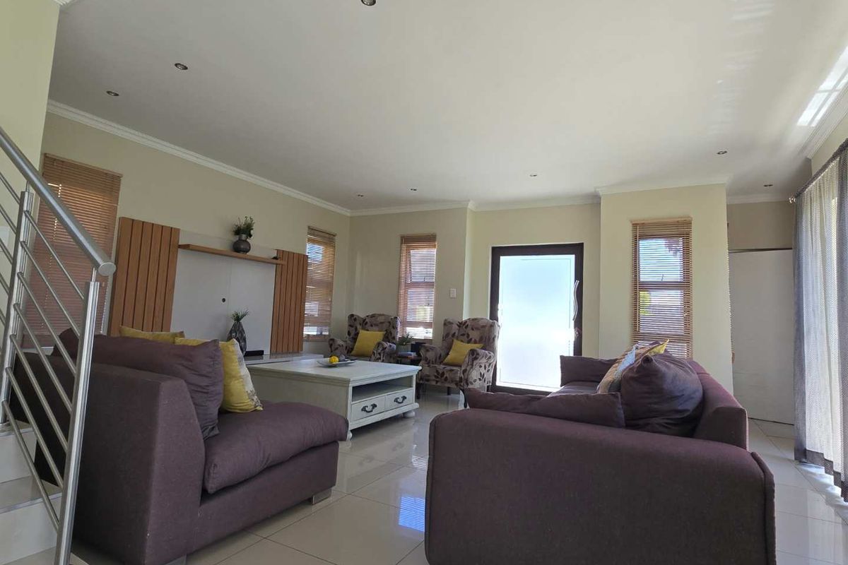 A spacious, well-lit living room featuring tiled flooring, recessed downlighting, and modern timber slat wall accents, creating a comfortable and inviting atmosphere.