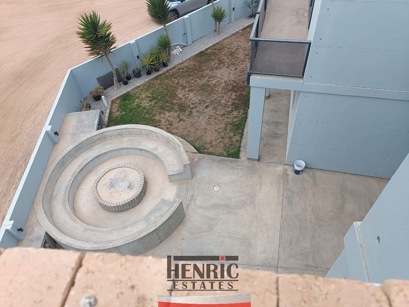 An elevated view of a rear garden featuring a built-in circular concrete fire pit, paved patio area, and perimeter boundary wall.