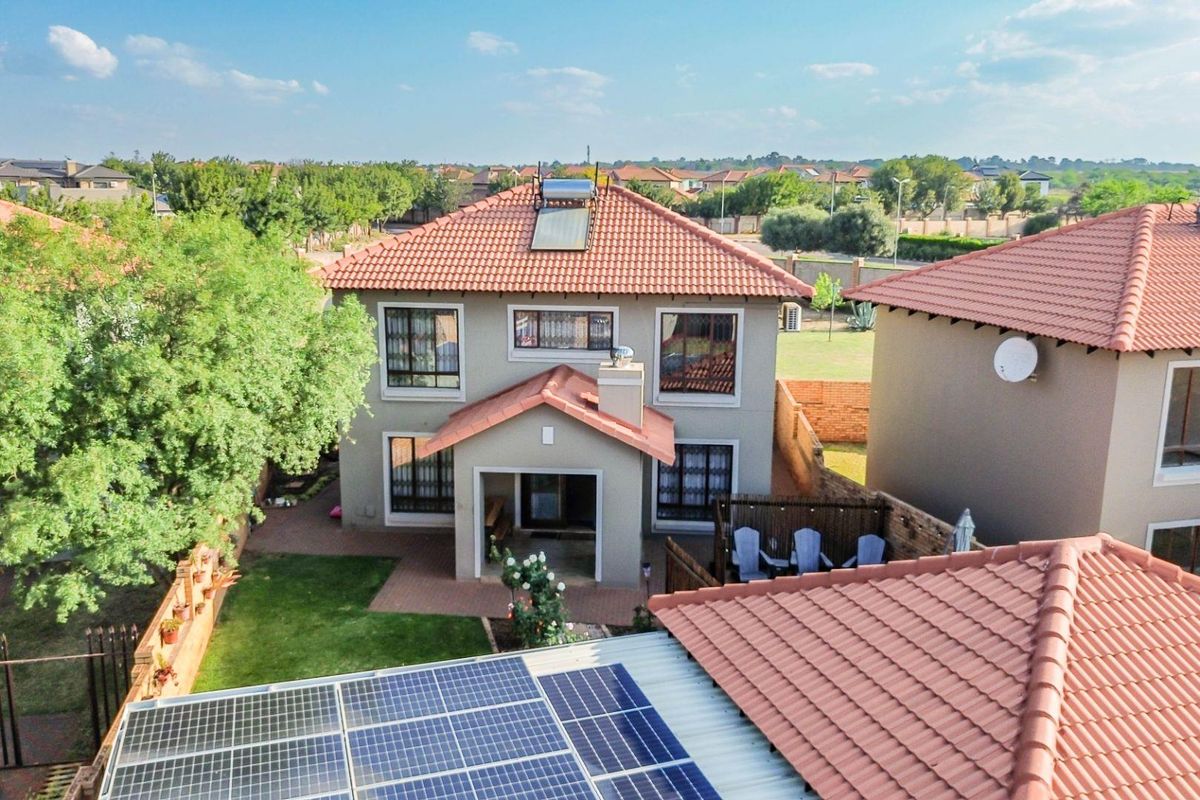 Aerial view of a two-story residential house featuring a tiled roof, solar water heating system, and solar panels, set within a landscaped garden.