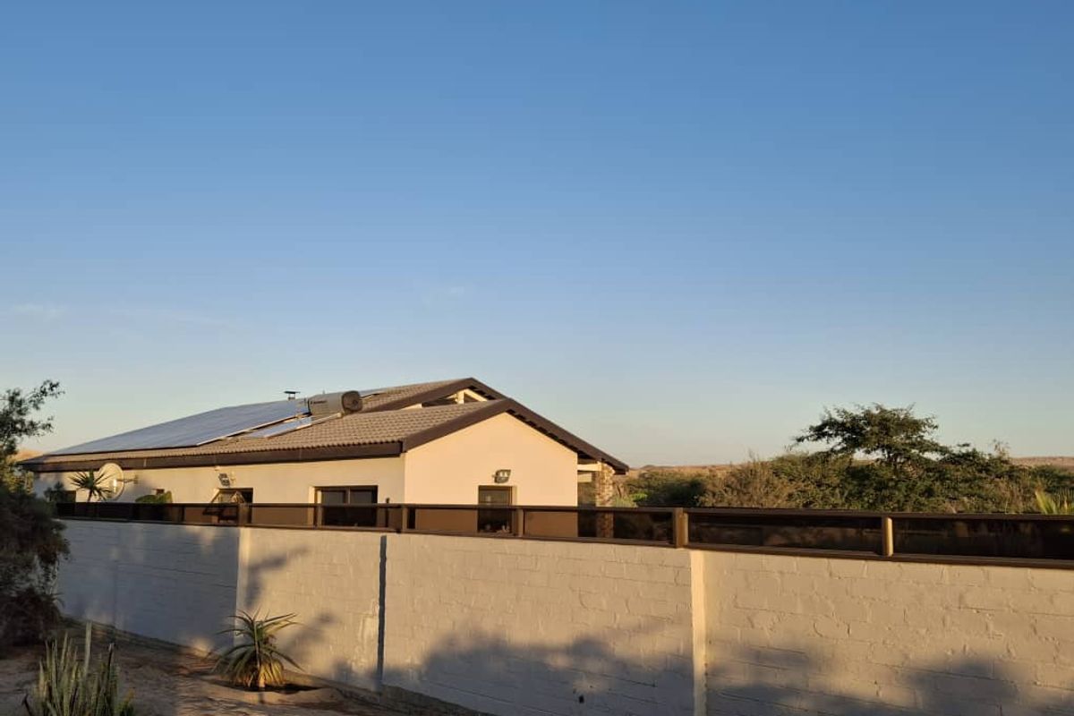 Rear view of the property featuring a tiled roof with installed solar panels and a solar geyser, enclosed by a secure boundary wall.