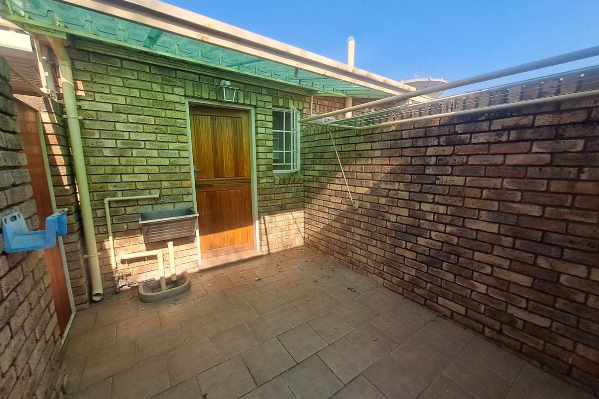 A private rear courtyard featuring exposed brick walls, paved flooring, a utility sink, and a covered drying area.