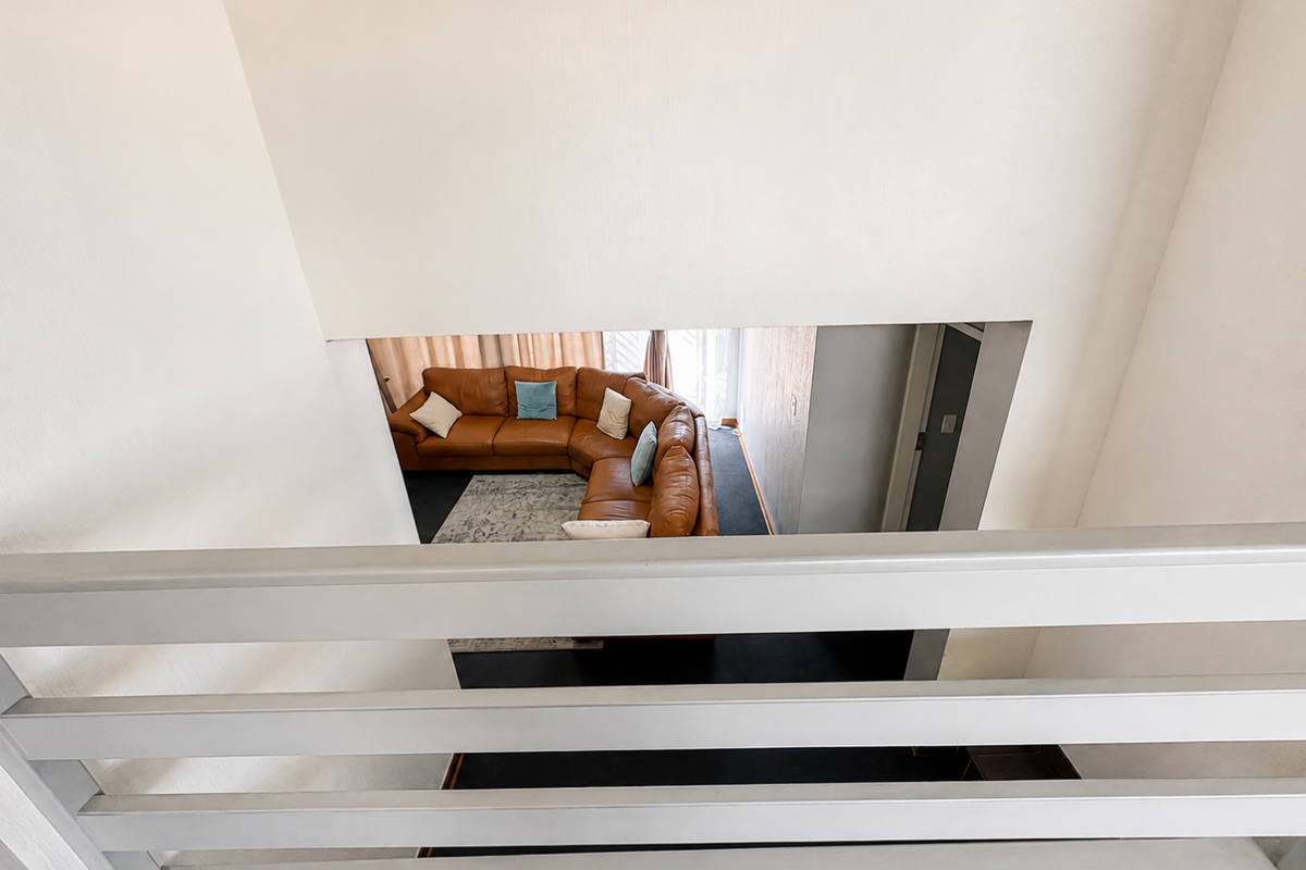 An elevated view looking down from a landing over a living area featuring a staircase railing in the foreground.